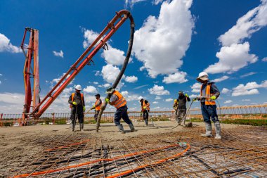 Lastik çizmeli inşaat işçisi pompa tüpünü doğru yöne yönlendiriyor, beton tabakası döküyor, betonu kare takviyesinin üzerine döküyor. Sıvı betonu sıkıştırmak için elektrikli alet, sıkıştırıcı kullanıyorlar.,
