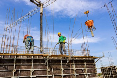 İnşaat işçisi çeliği güçlendiren sütunlar inşa etmek için kalıp içine beton dökmek için pompa tüpü kullanıyor. Mason taze sıvı betonu sıkıştırmak için elektrikli alet, sıkıştırıcı ve vibratör kullanıyor..