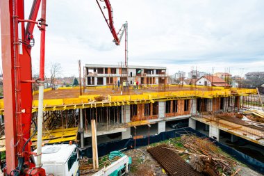 Pompa makineli kamyon ayakta duruyor, ahşap küf ve armatür çimento karışımı ile çıkış tübünü yönlendiriyor, taze beton tabakası, birinci kattaki iskan binasına, inşaat alanına.