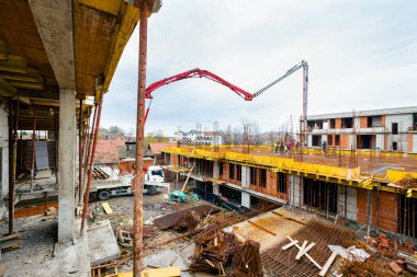 Pompa makineli kamyon ayakta duruyor, ahşap küf ve armatür çimento karışımı ile çıkış tübünü yönlendiriyor, taze beton tabakası, birinci kattaki iskan binasına, inşaat alanına.