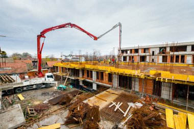 Pompa makineli kamyon ayakta duruyor, ahşap küf ve armatür çimento karışımı ile çıkış tübünü yönlendiriyor, taze beton tabakası, birinci kattaki iskan binasına, inşaat alanına.