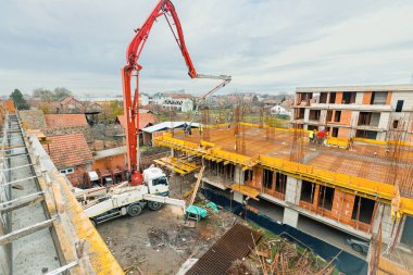Pompa makineli kamyon ayakta duruyor, ahşap küf ve armatür çimento karışımı ile çıkış tübünü yönlendiriyor, taze beton tabakası, birinci kattaki iskan binasına, inşaat alanına.