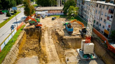 Kazı yaparken iki büyük kazıcının üstünde, yeni konut binası için kazı yapıyorlar ve birkaç çöp kamyonunu toprakla dolduruyorlar, inşaat alanında, proje devam ediyor.