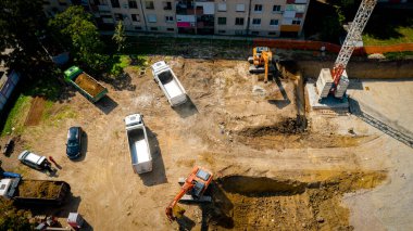Kazı yaparken iki büyük kazıcının üstünde, yeni konut binası için kazı yapıyorlar ve birkaç çöp kamyonunu toprakla dolduruyorlar, inşaat alanında, proje devam ediyor.