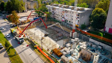 Şehir manzarasının üstünde, inşaat alanında, karıştırıcı kamyon pompa makinesine beton döküyor, genişletilmiş tüpe pompalanıyor, çalışan doğru yöne yöneliyor, bina temelinin katmanını, yapısını,.