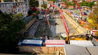 Şehir manzarasının üstünde, inşaat alanında, karıştırıcı kamyon pompa makinesine beton döküyor, genişletilmiş tüpe pompalanıyor, çalışan doğru yöne yöneliyor, bina temelinin katmanını, yapısını,.