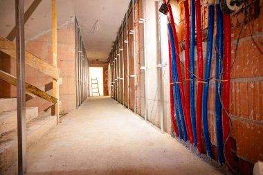 Uzun koridor boyunca bak. Duvara monte edilmiş dikey metal profiller, dağıtım sisteminin kırmızı ve mavi boruları, inşaat halindeki bir binanın zemin ısıtma sisteminin altında..