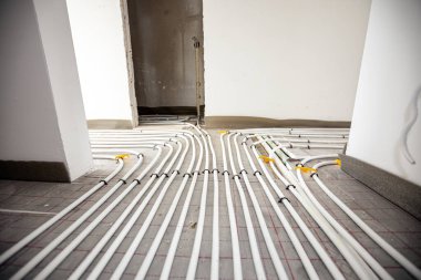 İnce beyaz borulara bak. Yeni pirincin karmaşık eğrisiyle bükülmüş, dağıtım sistemi manifoldları inşaat halindeki bir konut binasında merkezi ısıtma katı için monte edilmiş..