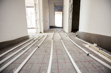 İnce beyaz borulara bak. Yeni pirincin karmaşık eğrisiyle bükülmüş, dağıtım sistemi manifoldları inşaat halindeki bir konut binasında merkezi ısıtma katı için monte edilmiş..