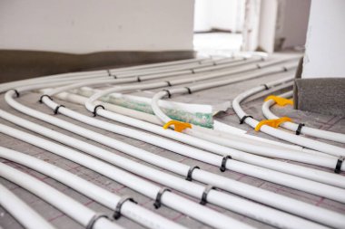 Yeni pirincin karmaşık eğrisinde bükülmüş ince beyaz boruların düşük açılı görüntüsü, inşaat halindeki bir konut binasında merkezi ısıtma katı için monte edilmiş dağıtım sistemi manifoldu.