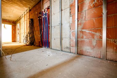 Uzun koridor boyunca bak. Duvara monte edilmiş dikey metal profiller, dağıtım sisteminin kırmızı ve mavi boruları, inşaat halindeki bir binanın zemin ısıtma sisteminin altında..