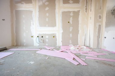 İnşaat alanında inşaat halindeki bölme duvarına elektrik kabloları ve delikleri olan kahverengi alçı tahtalarının ön görüntüsü. Pembe polistiren, köpük parçaları.