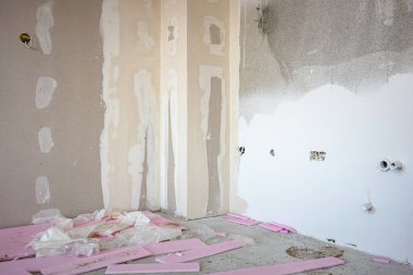 İnşaat alanında inşaat halindeki bölme duvarına elektrik kabloları ve delikleri olan kahverengi alçı tahtalarının ön görüntüsü. Pembe polistiren, köpük parçaları.