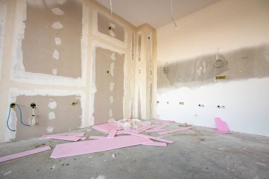 İnşaat alanında inşaat halindeki bölme duvarına elektrik kabloları ve delikleri olan kahverengi alçı tahtalarının ön görüntüsü. Pembe polistiren, köpük parçaları.