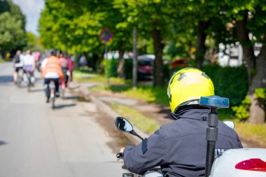 Polis memuru motosikletini tam üniformalı bir şekilde sürüyordu. Gruptaki insanları bisiklet sürerken, şehirde bisiklet sürerken, kalabalıkta sürüyordu. Trafikteki, kentsel çevredeki bisikletçiler için tehlike arz ediyordu.. 