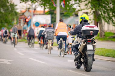 Polis memuru motosikletini tam üniformalı bir şekilde sürüyordu. Gruptaki insanları bisiklet sürerken, şehirde bisiklet sürerken, kalabalıkta sürüyordu. Trafikteki, kentsel çevredeki bisikletçiler için tehlike arz ediyordu.. 