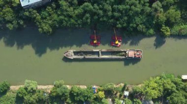 Üst manzaranın üzerinde, iki kazıcı aşağı doğru ilerler. Nehir, kanal, tortu, kirli bir su yolundaki çamurları tarar, tarar, temizler ve temizler..