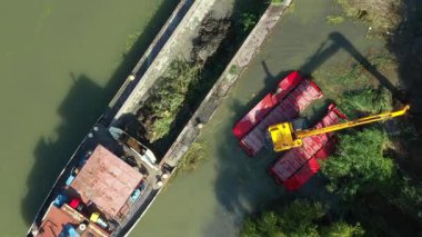 Üst manzarada, iki kazıcı yukarı doğru hareket eder. Nehir, kanal, tortuları derinleştirir ve kaldırır. Kirli bir su yolundaki çamurdan arınırlar..