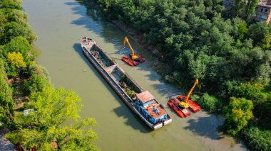 Nehir, kanal, derinleşen ve kirli bir su yolundaki tortu ve çamuru nehir yatağından kaldıran iki kazıcının üzerini tararken, tararken, tararken, tararken, tararken ve temizlerken.