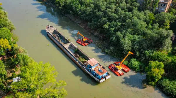 Nehir, kanal, derinleşen ve kirli bir su yolundaki tortu ve çamuru nehir yatağından kaldıran iki kazıcının üzerini tararken, tararken, tararken, tararken, tararken ve temizlerken.