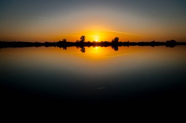 Akşamları güzel günbatımının manzarası gölün üzerinde, gölün üzerinde siluet suyun üzerinde ve bulutların sakin sularda yansıması.