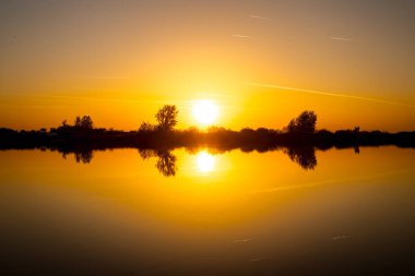 Akşamları güzel günbatımının manzarası gölün üzerinde, gölün üzerinde siluet suyun üzerinde ve bulutların sakin sularda yansıması.