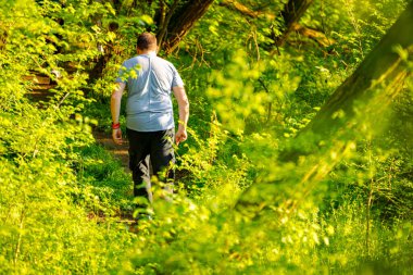 İnsanlar, aile, oğullarıyla birlikte orman patikasında yürüyen adamlar güneşli bir günde yaprak döken ağaçların arasına gidiyorlar. Küçük orman yolu, yol boyunca taze bahar bitkileri.