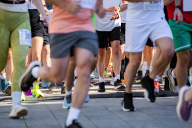 Büyük bir koşucu grubu, bir sokak maratonunda koşan sporcular, şehir yarışında koşan kalabalık, bacaklara ve ayaklara düşük açı bakan koşucular..