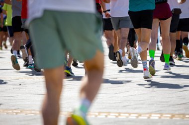 Büyük bir koşucu grubu, bir sokak maratonunda koşan sporcular, şehir yarışında koşan kalabalık, bacaklara ve ayaklara düşük açı bakan koşucular..