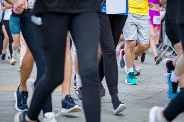 Büyük bir koşucu grubu, bir sokak maratonunda koşan sporcular, şehir yarışında koşan kalabalık, bacaklara ve ayaklara düşük açı bakan koşucular..
