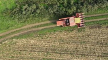 Üst görünümde, doli hareketi kırmızı kombinasyonu takip ediyor, kırsal yoldaki tarımsal alanlar arasında giden hasat makinesi, tozlu zemin yolunda seyahat ediyor..