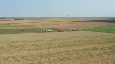 Yukarıda, Dolly harvester 'ı tarımsal tarlalar arasında kırsal yolda giderken, tozlu toprak yolda giderken takip ediyor. Römorklu iki traktör aynı yolda gidiyor.