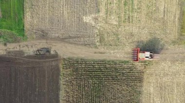 Üst tarafta, tarımsal tarlalar arasında kırsal yolda giden hasat makinesi, tozlu toprak yolda ilerliyor..