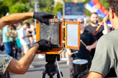 Fotoğrafçı insanların fotoğraflarını çekiyor, ahşap ve metalden yapılmış eski model retro kamera kullanıyor, ahşap kutu tasarımı, modern profesyonel tripodlar üzerinde kentsel alandaki halk etkinliklerinde,.