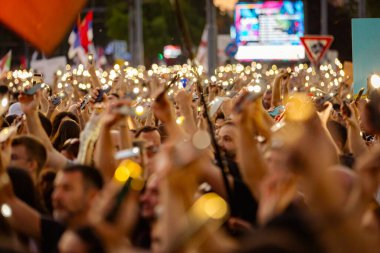 Bulanık, belirsiz pek çok insan el kaldırıyor cep telefonu, fenerli cep telefonu, kurbanları onurlandıran ışık, Sırbistan 'da çatı çökmesi ve tren istasyonunda kaybedilen hayatlar için 16 dakikalık sessizlik.