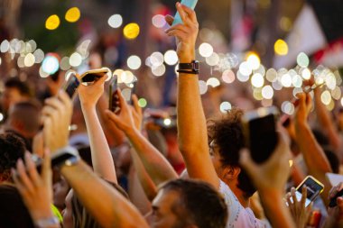 Bulanık, belirsiz pek çok insan el kaldırıyor cep telefonu, fenerli cep telefonu, kurbanları onurlandıran ışık, Sırbistan 'da çatı çökmesi ve tren istasyonunda kaybedilen hayatlar için 16 dakikalık sessizlik.