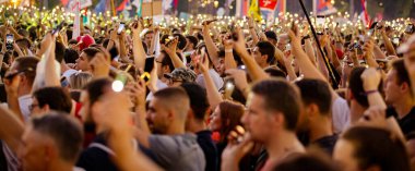 Bulanık, belirsiz pek çok insan el kaldırıyor cep telefonu, fenerli cep telefonu, kurbanları onurlandıran ışık, Sırbistan 'da çatı çökmesi ve tren istasyonunda kaybedilen hayatlar için 16 dakikalık sessizlik.