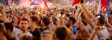 Bulanık, belirsiz pek çok insan el kaldırıyor cep telefonu, fenerli cep telefonu, kurbanları onurlandıran ışık, Sırbistan 'da çatı çökmesi ve tren istasyonunda kaybedilen hayatlar için 16 dakikalık sessizlik.