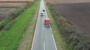 Above top view, dolly move over worker cutting weed among road signs with hand mower, motor signage grass trimmer, edger. Service truck with trailer carry traffic signs for road works