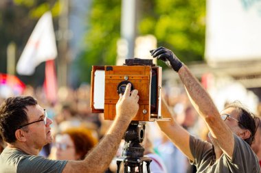 Belgrade, Serbia - June 28, 2025: Photographer is taking photo of people, using old vintage retro camera, made of wood and metal, wooden box design, on modern professional tripod at public event.