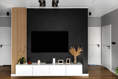 Oturma odasında beyaz bir duvarın üzerinde asılı bir TV olan siyah mat televizyon duvarı..