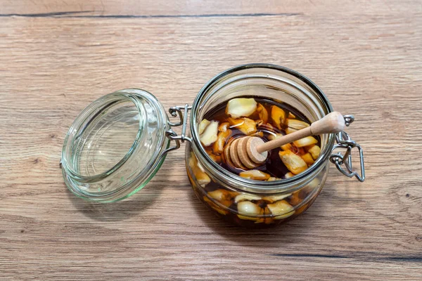 Garlic with honey in a glass jar on the kitchen counter with a wooden honey stick.