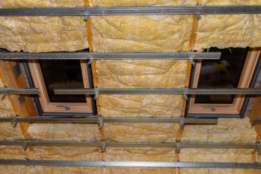 Aluminum frame with hangers placed on beams in the attic for mounting plasterboards, visible roof window.