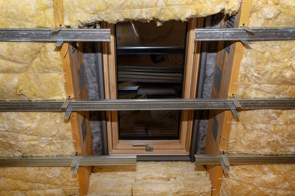 Aluminum frame with hangers placed on beams in the attic for mounting plasterboards, visible roof window.