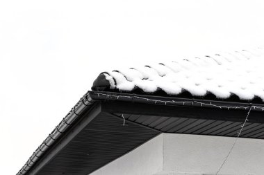 Tek bir ailenin çatısı bulutlu bir gökyüzüne karşı karla kaplıdır. Çatıda görünen bir kiremit ve düşen bir kar..