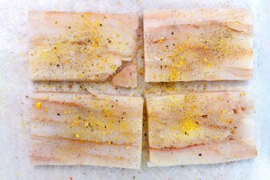 Fresh cod fillet cut into squares, sprinkled with spices lying on a paper towel, top view.