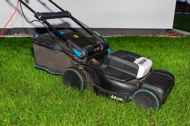 Electric lawn mower with electric drive with a cutting width of 44 centimeters standing on the lawn in the evening.