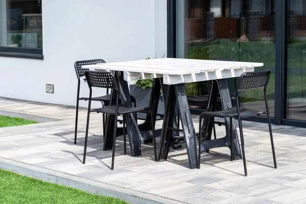 stock image Terrace table made of white pallet standing on plastic trestles, black plastic chairs.
