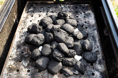 Lighting a home grill with charcoal and white kindling for the grill, standing in the home garden