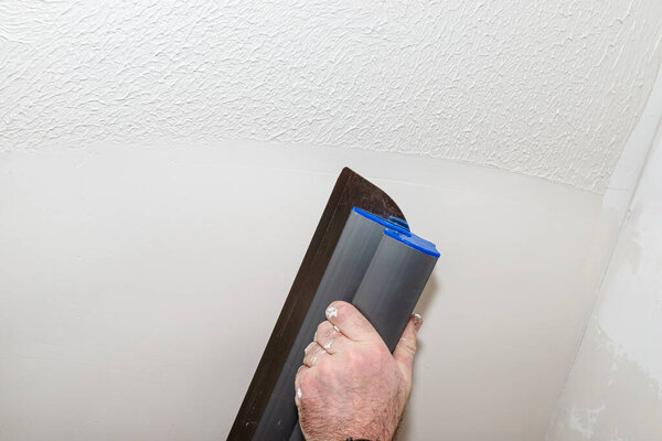 A man applies ready-made polymer plaster from a bucket using special plaster cutters.